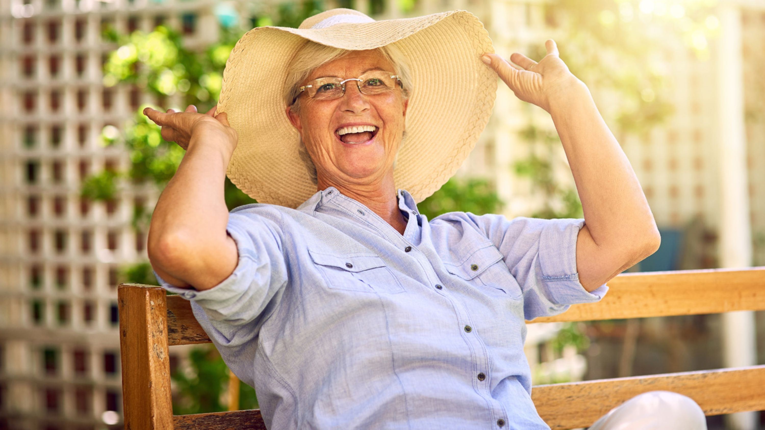 Un'anziana signora con un cappello siede su una panchina del parco in estate.