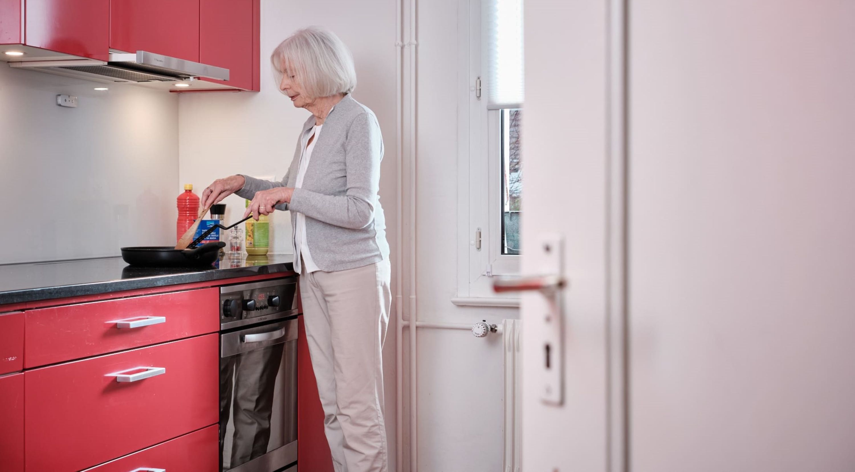 Eine Seniorin steht in ihrer Küche und kocht.