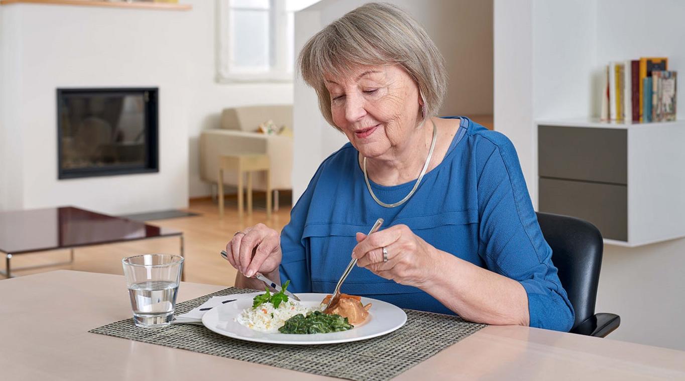 Eine Seniorin ist in ihrem Wohnzimmer am Essen
