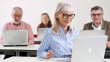 Une femme âgée portant des lunettes est assise devant son ordinateur dans son bureau.