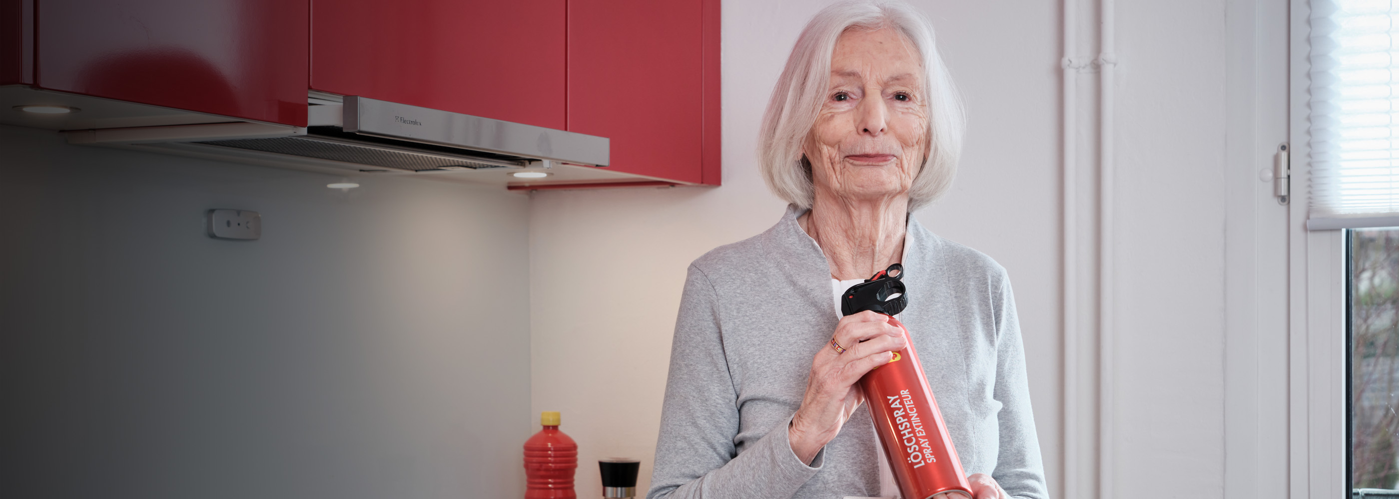Ältere Dame mit Löschspray in der Küche
